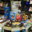 Table display at the UC Davis bookstore with travel books on countries like India, Thailand and China. Several UC Davis Gunrock plush toys are scattered among the books.