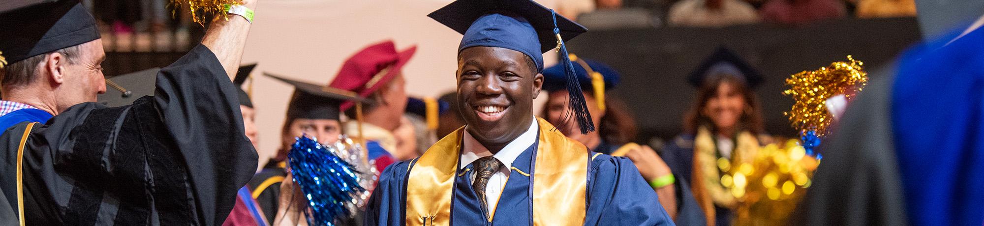 A UC Davis male graduate in cap and gown is celebrated by faculty, also in caps and gowns, at the 2023 commencemement.